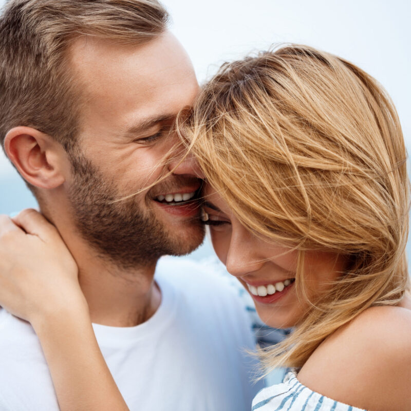 Young beautiful couple smiling, laughing, rejoicing sea background